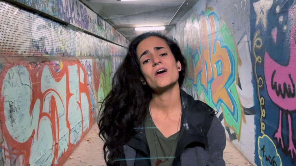 Beast & Beauty, Frau mit offenen Haaren singt im Tunnel mit Graffiti bemalten Wänden
